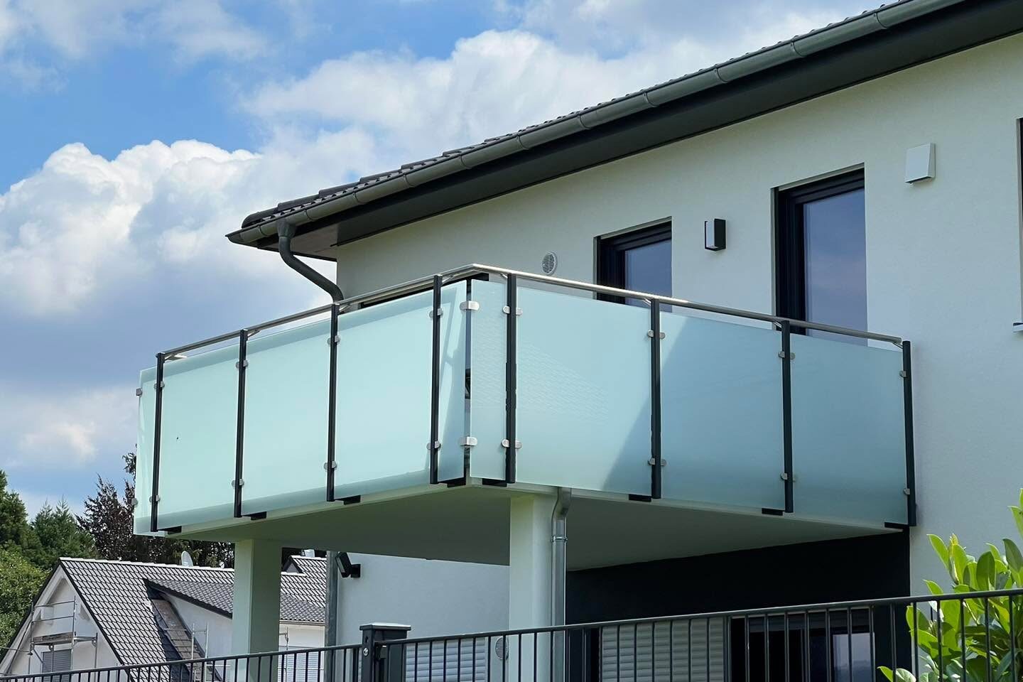 Auskragender Balkon mit Glasgeländer an einem weißen Wohnhaus