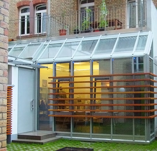 Wintergarten aus Stahl und Glas mit Holzlamellen an einer Altbaufassade